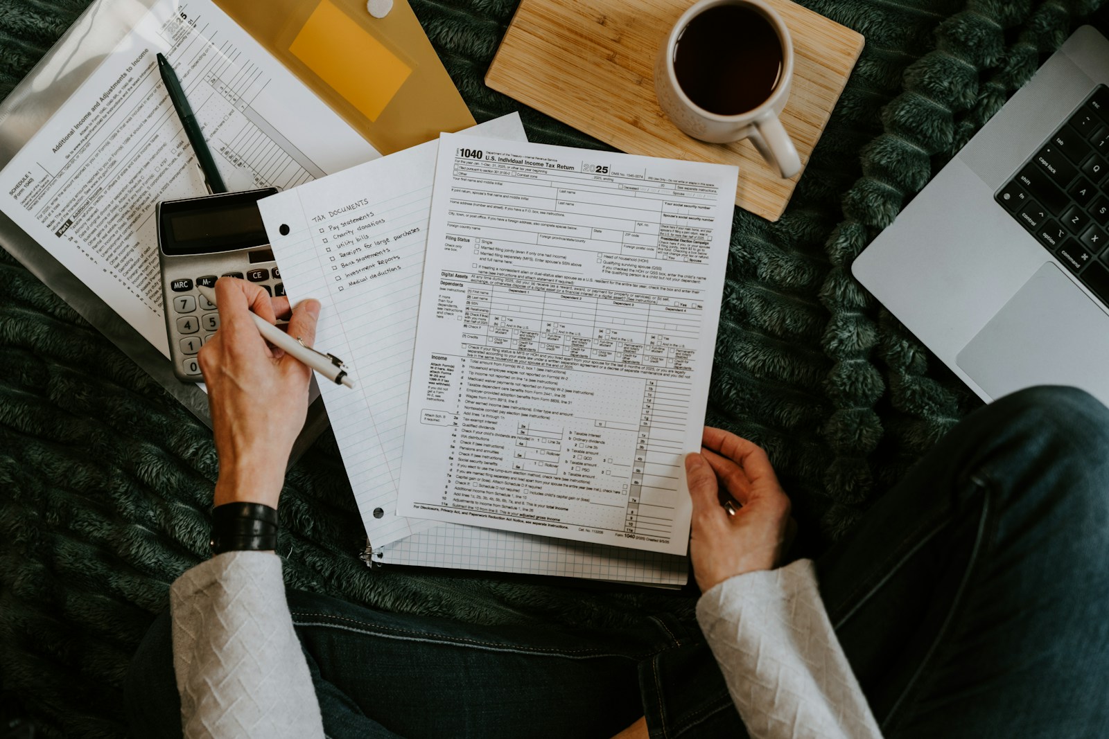 Personne examinant des documents avec une calculatrice et un ordinateur portable
